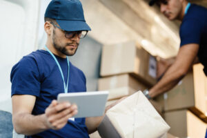 young-delivery-man-using-touchpad-while-reading-label-package